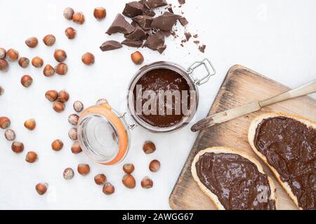 Homemade vegan hazelnut chocolate spread on sourdough bread and in a kilner jar, with unshelled hazelnuts and chunks of dark chocolate Stock Photo