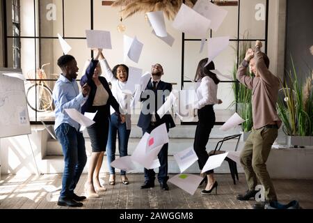 Diverse staff throwing papers up celebrating corporate success feels overjoyed Stock Photo
