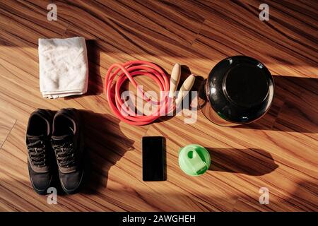Belongings of sportsman on wooden floor: sneakers, skipping rope, shaker with protein cocktail, smartphone and towel Stock Photo