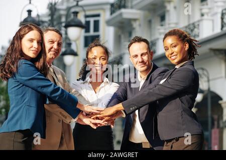Positive multi-ethnic business team stacking hands to express support and unity Stock Photo