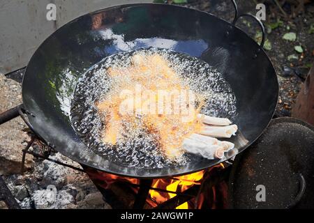 Close-up of asian spring rolls frying in hot oil in a wok frying pan on a traditional fire place in a philippine home, called dirty kitchen Stock Photo