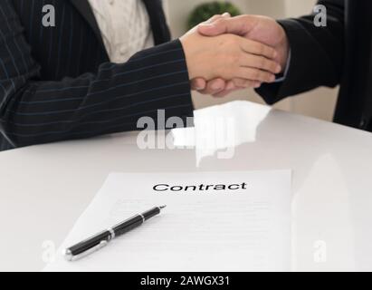 Close-up contract document with image of a firm handshake between two business partners signing a contract in background. Stock Photo