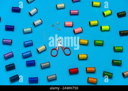 top view creative still life flat lay with reels of multicolored threads and scissors pattern on a blue background Stock Photo