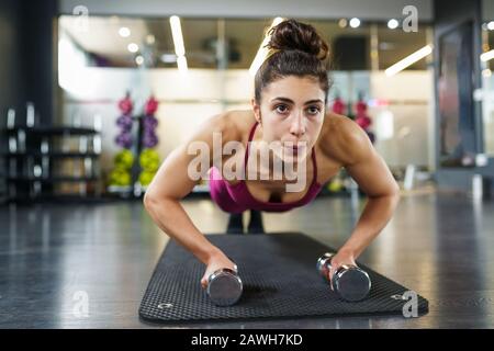 Woman doing push-ups exercise with dumbbell in a fitness workout