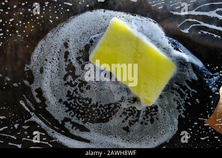Hand in a black glove washes the glass with a foam sponge with foam on a dark background. Stock Photo