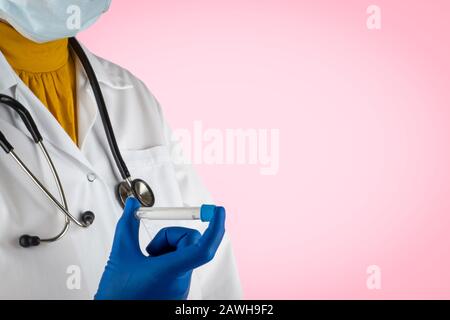 Stethoscope and doctor hands holding specimen bottle on pink background. Selective focus and crop fragment Stock Photo