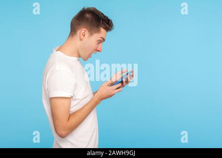 Side view of amazed astonished man in t-shirt using cellphone with surprised expression, shocked by message in social network, mobile communication. i Stock Photo