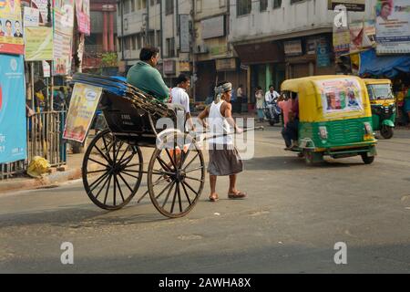 Man rickshaw puller is pulling his hand rickshaw with passenger on the street in Kolkata. India Stock Photo