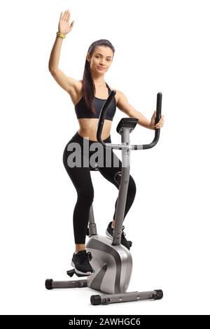 Young female exercising on a stationary bike and waving isolated on white background Stock Photo