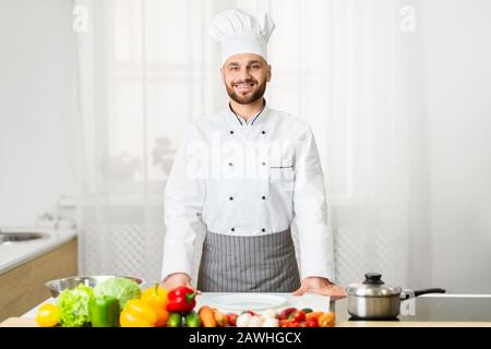 Male Chef In Uniform Smiling Standing In Kitchen Stock Photo