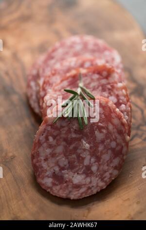 Sliced salame milano sausage on olive wood board with rosemary, shallow focus Stock Photo