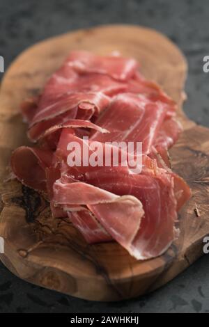 Sliced prosciutto ham on olive wood board, shallow focus Stock Photo