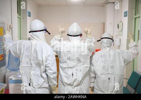 (200209) -- CHANGSHA, Feb. 9, 2020 (Xinhua) -- Yi Junfeng (L), together with his colleagues Zhang Yao (C) and Yang Caixia, display handwritings on their protective suits in support of the battle against the novel coronavirus outbreak, at Hunan People's Hospital in Changsha, central China's Hunan Province, Feb. 7, 2020. Amid the current novel coronavirus outbreak, 22-year-old male nurse Yi Junfeng has volunteered to join the battle against the epidemic. After a series of professional trainings, he now works as a front-line fever clinic nurse at Hunan People's Hospital in Changsha. Yi believes t Stock Photo