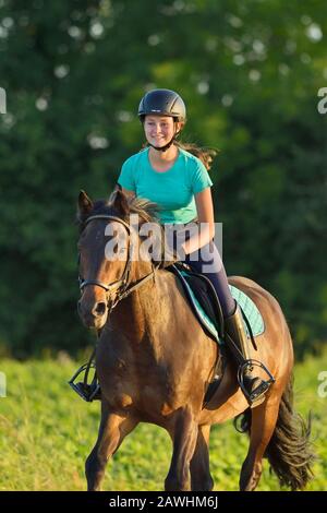 Girl on back of a German pony cantering on a German pony in a stubble field in the evening Stock Photo