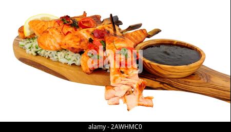 Grilled salmon skewers with rice on an olive wood serving board isolated on a white background Stock Photo