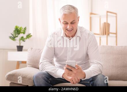 Cheerful aged man using smartphone at home Stock Photo
