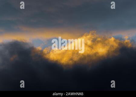 Fluffy clouds illuminated by disappearing rays at sunset and dark thunderclouds floating across sunny blue sky to change season weather. Stunning view Stock Photo