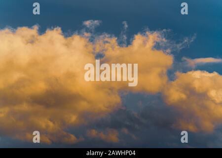 Stunning fluffy thunderstorm clouds illuminated by disappearing rays at sunset and dark cumulonimbus floating across sunny blue sky to change season w Stock Photo