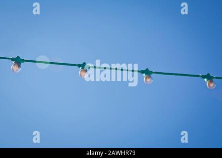 lamps in series with the blue sky background . Green electric bulb on a wire with blue sky in background . Street electric garland against the sky Stock Photo