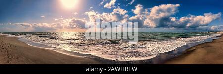 Amazing panoramic view from sandy beach to horizon,  with dramatic lights over rough sea and wonderful dark blue sky with scenic cumulonimbus clouds a Stock Photo