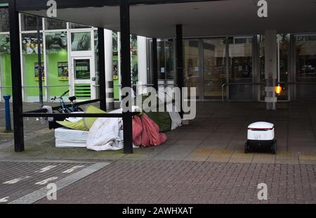 Tents of the homeless in Central Milton Keynes with a Starship delivery robot. Stock Photo