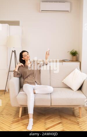 Young woman switching on air conditioning at home Stock Photo