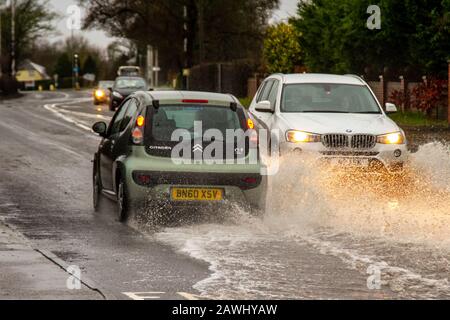 A car passing through flood at waters speed throwing up spray on a road in Kirkham, Lancashire, UK. Feb, 2020. UK Weather;  Storm Ciara roads flooded in Kirkham. Credit: MediaWorldImages/Alamy Live News Stock Photo