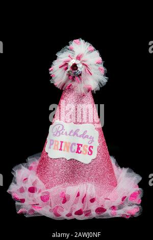 A pink glittery party hat with the words birthday princess on it isolated on a black background Stock Photo