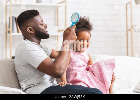 Loving black father brushing his cute daughter hair Stock Photo