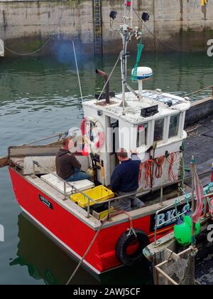 Two Fishermen at the stern of a small Inshore Fishing Boat moored up in Seahouses Harbour in Northumberland. Stock Photo