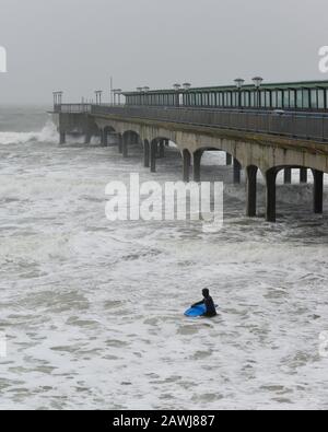 Surfer in rough sea with big waves from Storm Ciara at Boscombe Pier, Bournemouth, Dorset England, UK, February Stock Photo