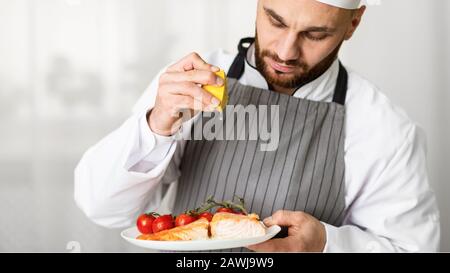 Cook Man Plating Salmon Steak Squeezing Lemon Standing In Kitchen Stock Photo