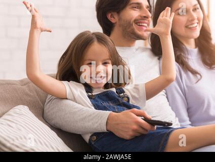 Joyful Little Girl Raising Hands And Smiling Next To Parents Stock Photo