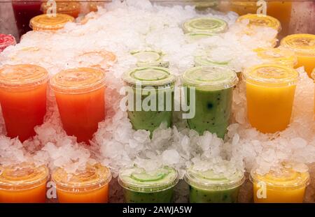 Cold refreshing fruit drinks in various flavors and colors, kept in transparent plastic cups, placed in ice cubes. Series of 3. Stock Photo