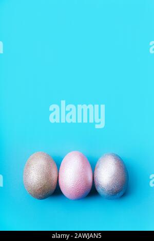 Three colored chicken eggs of pink, silver, golden on blue color background  Stock Photo