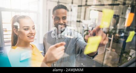 Business people meeting at office and use post notes to share idea. Brainstorming concept. Sticky note on glass wall. Stock Photo