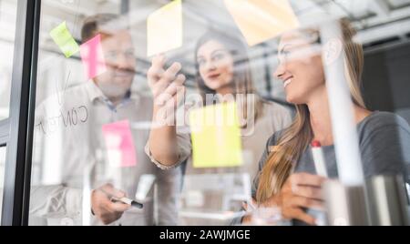 Business people meeting at office and use post notes to share idea. Brainstorming concept. Sticky note on glass wall. Stock Photo