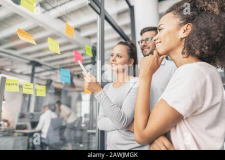 Business people meeting at office and use post notes to share idea. Brainstorming concept. Sticky note on glass wall. Stock Photo