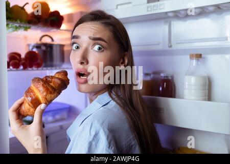 Hungry girl opening fridge, eating baking late in night Stock Photo