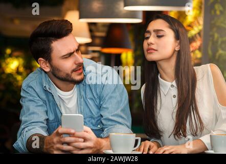 Girlfriend Reading Boyfriend's Messages While He Texting Sitting In Cafe Stock Photo