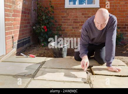 Builder laying and grouting York stone paving slabs outdoors, DIY home patio project , UK Stock Photo