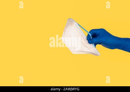 Hands holding protection medical mask on yellow background. Healthcare and copy space concept Stock Photo