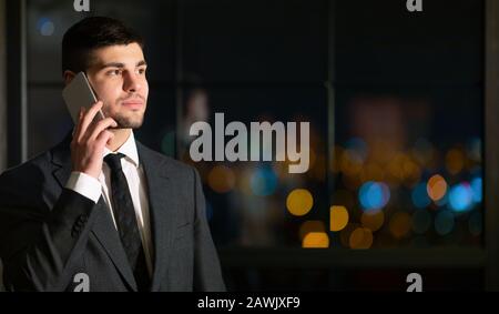 Businessman Talking On Mobile Phone Standing In Night Office Stock Photo