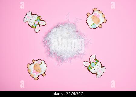 From above view of glazed cookies isolated on pink background. Easter ginger cookies in shape of two bunnies in wreaths and two sheep around white nest. Spring and easter holidays concept. Stock Photo