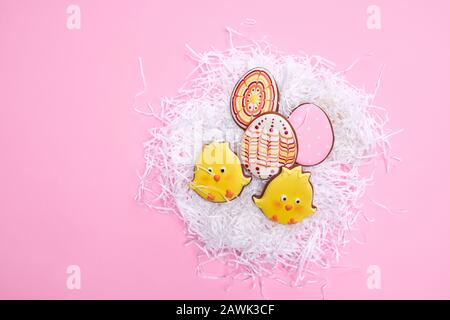From above view of glazed cookies in shape of two lovely yellow chicks and colorful eggs lying in white nest isolated on pink background. Close up of cute pastry. Spring and easter holidays concept. Stock Photo