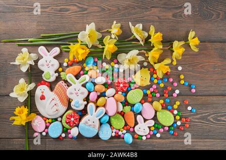 From above view of colorful ginger glazed cookies and chocolate balls and daffodils isolated on wooden background. Homemade lovely delicious pastry in shape of easter animals, eggs and red flowers. Stock Photo