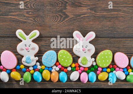 From above view of big and small peanut chocolate balls in crispy sugar shell isolated on wooden background. Close up of easter ginger glazed cookies in shape of two bunnies and eggs in row. Stock Photo
