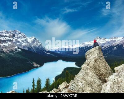 Peyto Lake, Banff National park in Canada with the Canadian Rockies in the distance, and a woman sat on a rock in the foreground with pink hair Stock Photo