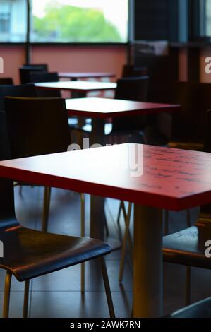 interior design with red tables and wooden chairs, against the background of windows with daylight, selective focus Stock Photo