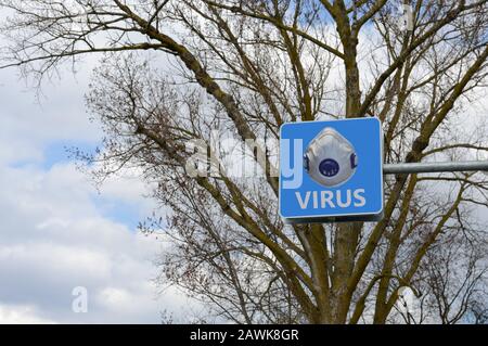 warning sign with the word "virus" and the image of a respiratory mask filter on a background of trees, sky and clouds Stock Photo